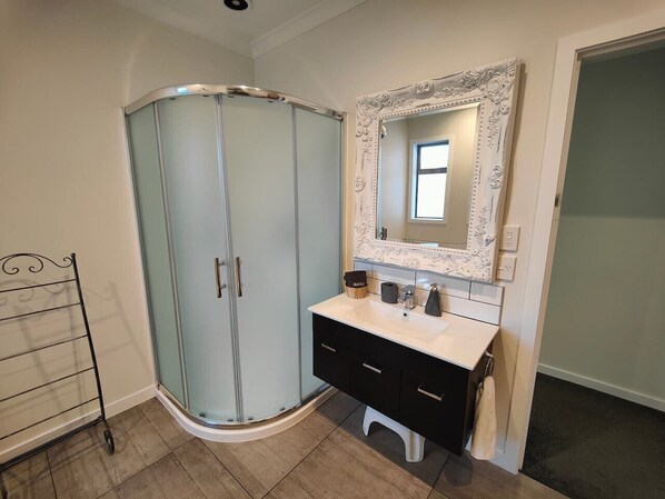A bathroom with a glass shower enclosure, a white vanity with black drawers, and a large mirror with an ornate frame. - Church Street Charmer (Riverton / Aparima)