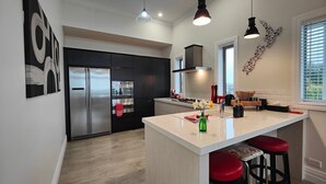 Een moderne keuken met een groot kookeiland, roestvrijstalen apparatuur en rode barstoelen.
