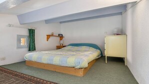 A single-bed room with a sloped ceiling, a small bedside table, a nightstand, a cabinet, and a window with a curtain. - STUDIO MEZZANINE CLIMATISE POUR 4 PERSONNES (LE CAP D AGDE)