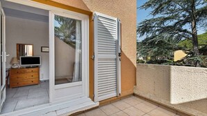 A room with a sliding glass door leading to a balcony, a wooden dresser, and a television. - STUDIO MEZZANINE CLIMATISE POUR 4 PERSONNES (LE CAP D AGDE)