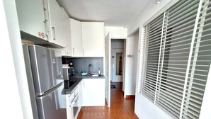 A compact kitchen with white cabinets, a stainless steel refrigerator, and a tiled floor. - STUDIO CABINE CLIMATISE AVEC CHAMBRE ALCÔVE (LE CAP D AGDE)