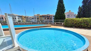 A round swimming pool with a tiled edge, surrounded by a low wall and a hedge. - STUDIO CABINE CLIMATISE AVEC CHAMBRE ALCÔVE (LE CAP D AGDE)