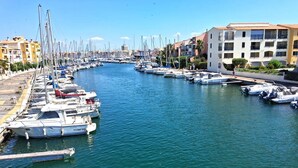 A marina with boats docked along a waterfront, buildings on the right, and a clear sky. - STUDIO CABINE CLIMATISE AVEC CHAMBRE ALCÔVE (LE CAP D AGDE)