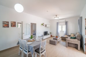 Un salon moderne comprenant un coin repas, un ensemble de canapés, un téléviseur et une petite table agrémentée d’une plante.