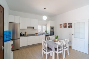 Une cuisine moderne avec des meubles blancs, un réfrigérateur en acier inoxydable, un four à micro-ondes et un coin repas comprenant une table et des chaises.