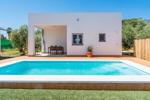 Une maison moderne dotée d’une piscine, d’une terrasse avec une table et des chaises, et d’un petit jardin.
