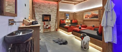 Ein moderner Spa-Bereich mit einer Steinsinnette, Holzmöbeln, einem Kamin und einer Couch mit roten Kissen.