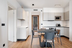 Una cocina moderna con muebles blancos, un microondas empotrado y un comedor con mesa y sillas.