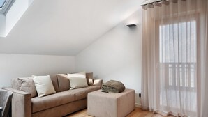 Una sala de estar moderna con sofá, reposapiés y cortinas de gasa.