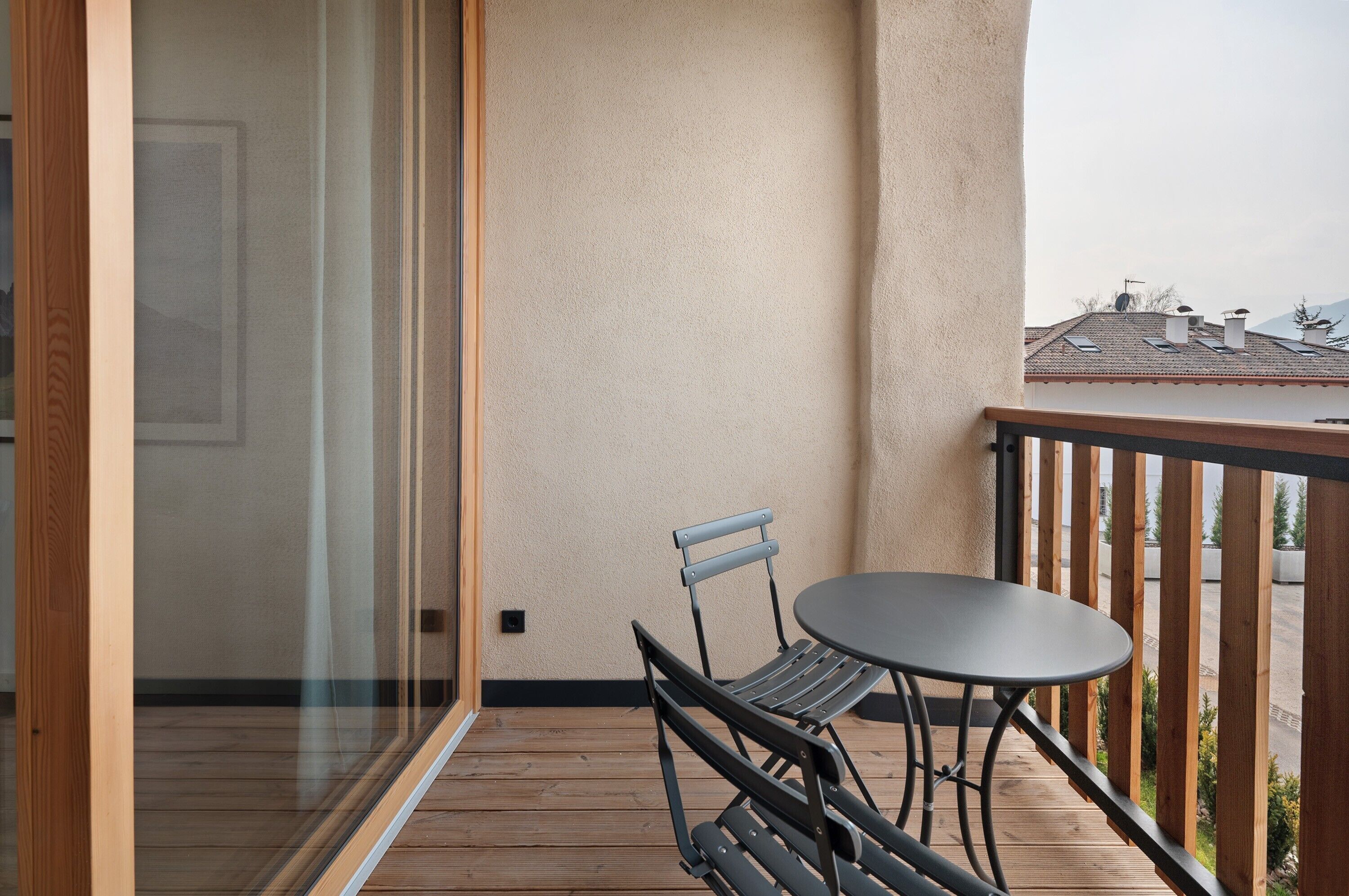 Un balcone con tavolo e sedie, un pavimento in legno e vista su un edificio con tetto in tegole.