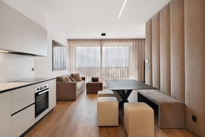 A modern kitchen with a dining area, a sofa, and a large window with curtains.