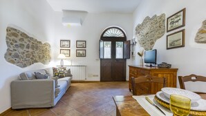 A living room with a sofa, a dining table with plates and a glass, a TV, and a stone wall. - Apartment 'Ulivo' with Mountain View, Wi-Fi and Air Conditioning (Terrazze)