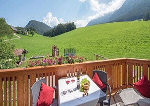 Una terraza con una mesa para dos, vista a un campo verde y una montaña al fondo.