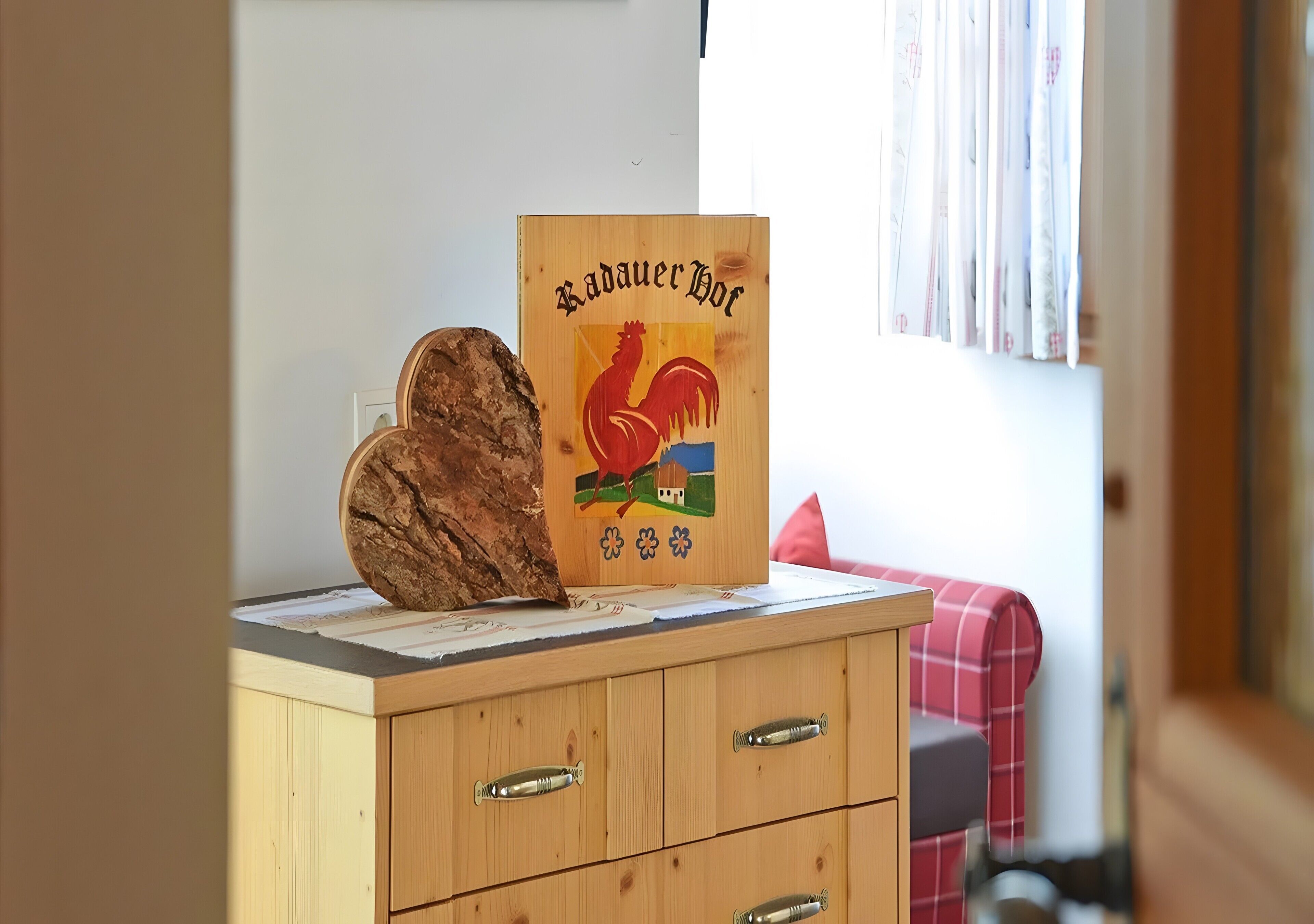 A wooden cabinet with drawers, a wooden sign with a rooster, and a red plaid cushion.