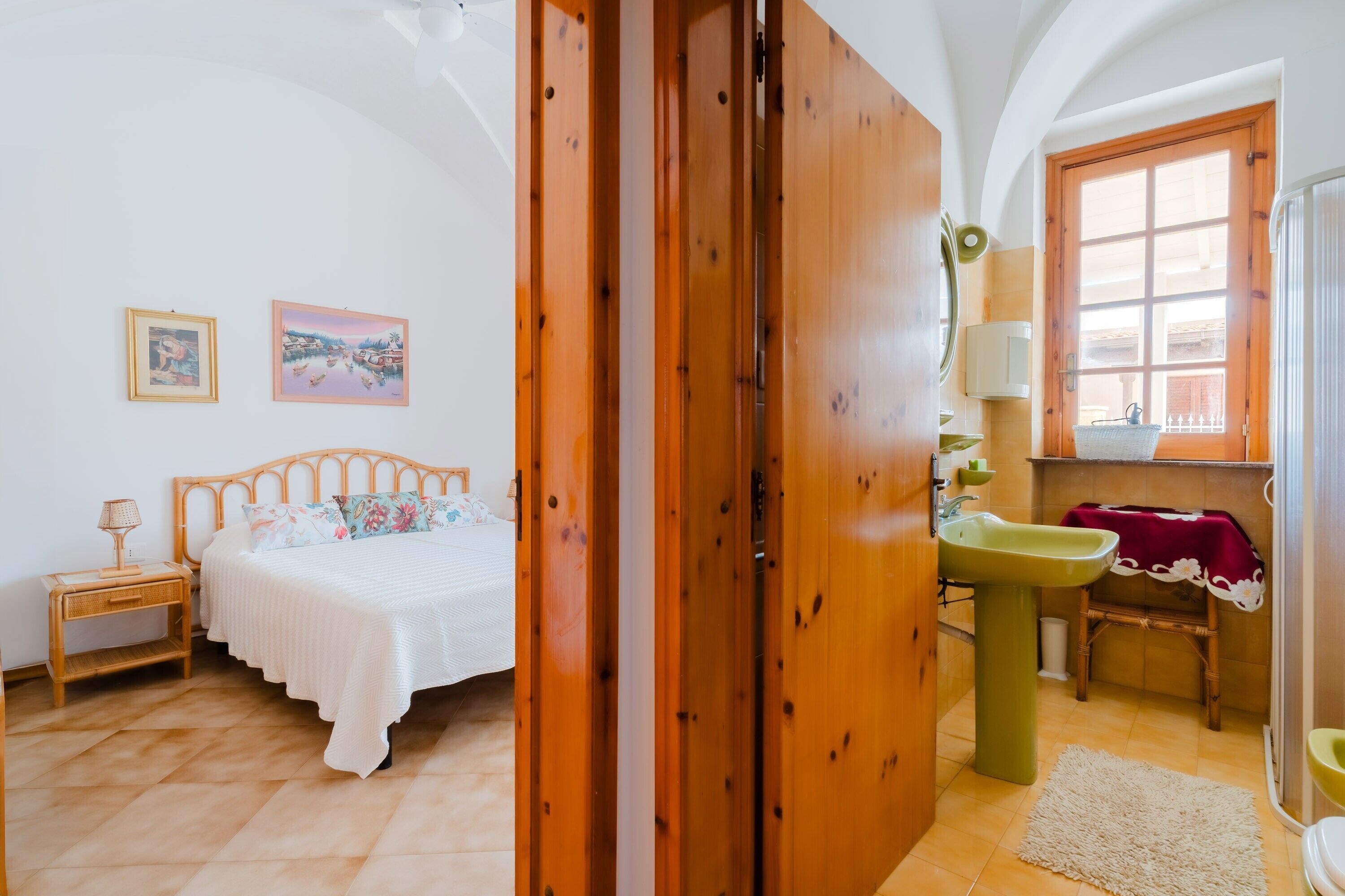 Une chambre à coucher avec un lit, une armoire en bois, une salle de bain avec un lavabo et un miroir, et deux tableaux encadrés accrochés au mur.