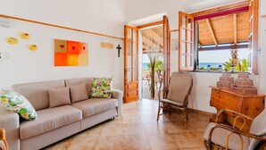 Ein Wohnzimmer mit Sofa, Sesseln, einem Holzschrank und Meerblick durch ein Fenster.