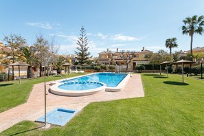 A swimming pool surrounded by a well-maintained lawn, with a clear sky and residential buildings in the background. - Holiday Home 'Playa Carabassi' with Shared Pool, Private Terrace and Wi-Fi (Santa pola)