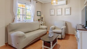 Un salon comprenant un canapé, un fauteuil, une petite table et un téléviseur.
