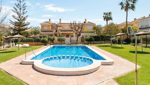 Une piscine dotée d’une terrasse carrelée, entourée d’une pelouse bien entretenue et, au fond, d’un immeuble à plusieurs étages.