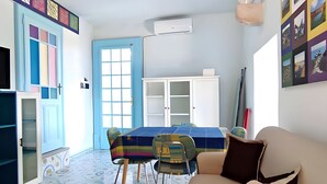 Een kamer met een blauwe deur, een witte kast, een bank, een tafel met stoelen en een vloer met een patroon.