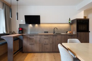 A modern kitchen with wooden cabinets, a built-in oven, and a dining area with a table and chairs. - Apartment ‘Charly’ with Mountain View, Private Garden, and Wi-Fi (San Martino)