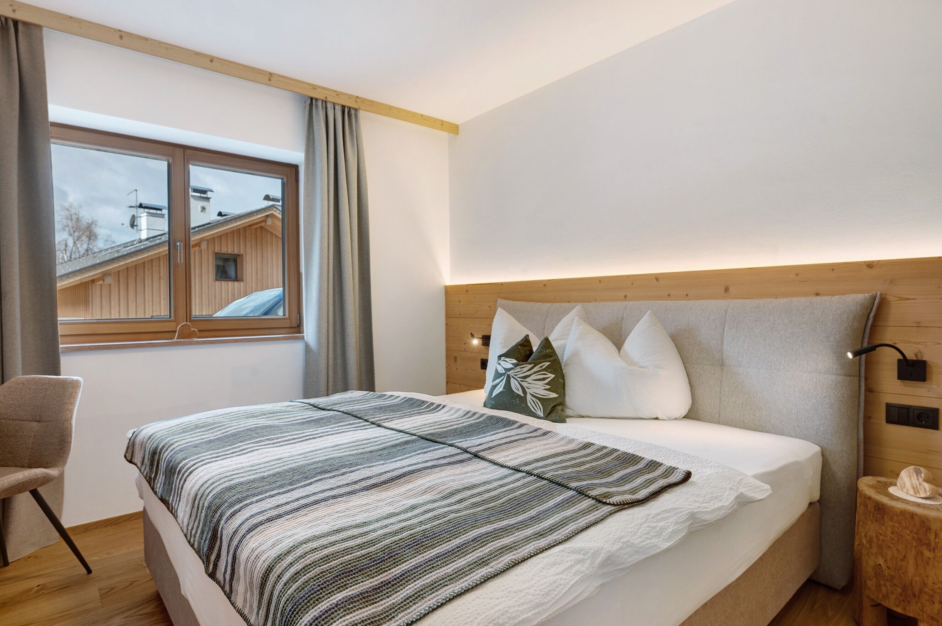 A bedroom with a bed, a chair, a nightstand, a window, and a view of a building outside.