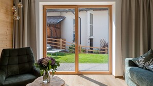 A room with a sliding glass door leading to a patio, a green sofa, a small round table with a vase, and a wooden ceiling. - Apartment ‘Charly’ with Mountain View, Private Garden, and Wi-Fi (San Martino)