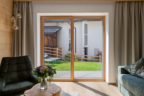 A room with a sliding glass door leading to a patio, a green sofa, a small round table with a vase, and a wooden ceiling.
