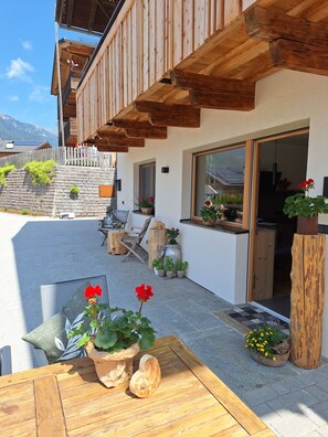 A wooden deck with a table and chairs, potted plants, and a view of a mountain. - Apartment ‘Charly’ with Mountain View, Private Garden, and Wi-Fi (San Martino)