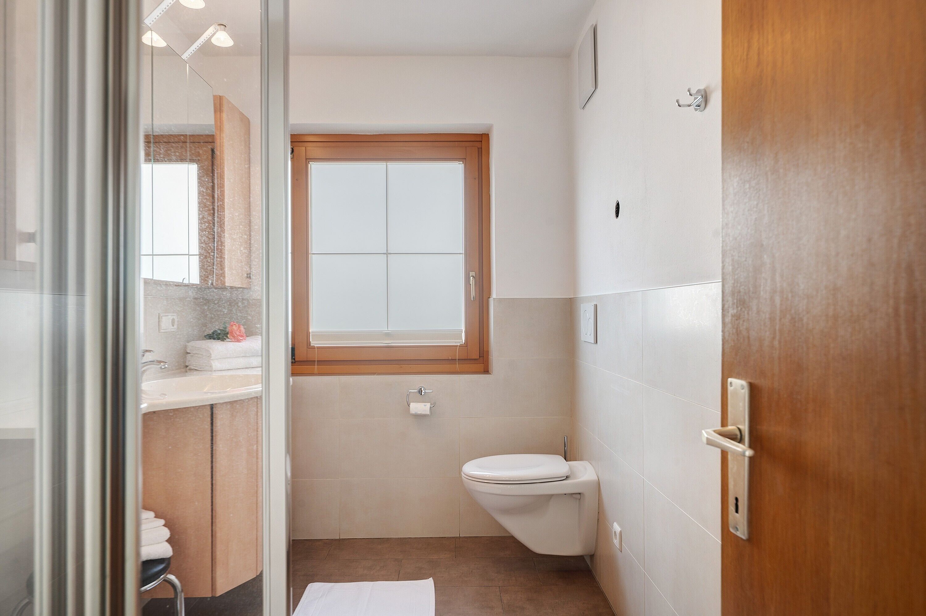 Une salle de bain avec des toilettes, un lavabo, une fenêtre et une porte en bois.