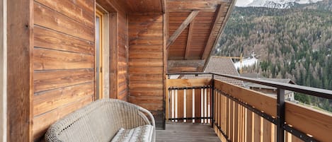 A wooden balcony with a wicker chair, wooden railings, and a mountainous view.