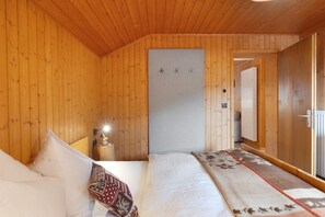 Habitación con paneles de madera, una cama, mesita de noche, calentador en la pared y una puerta que da a otra habitación.