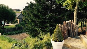 Un jardin avec une terrasse en bois, un arbre en pot et un mur de pierres.