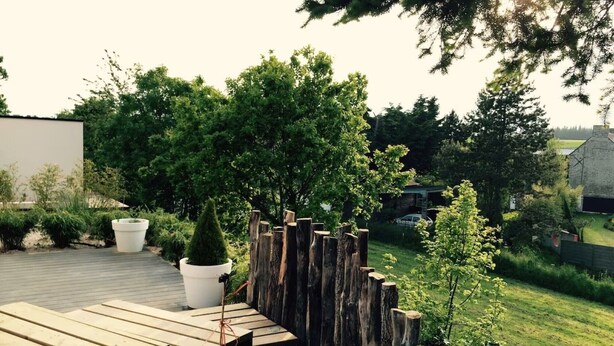 Une terrasse en bois agrémentée d’une clôture rustique, de plantes en pot et offrant une vue sur un paysage verdoyant.