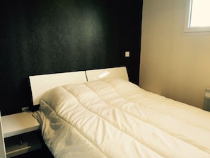 Cama com cabeceira branca e um único travesseiro branco.