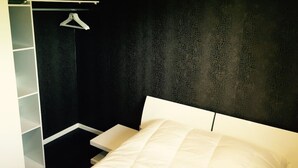 Une chambre à coucher avec un lit, une armoire blanche et une tringle pour suspendre les vêtements.