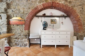 Une pièce avec un mur en pierre, une commode blanche, un banc et un ventilateur.