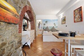 Une pièce avec un mur en pierre, un lit, une table à manger et une fresque représentant une scène de plage.