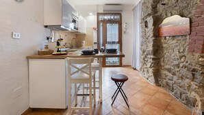 Una cocina con un refrigerador blanco, una isla de madera, una silla blanca, un taburete pequeño y una pared de piedra.