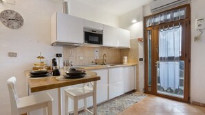 Una cocina con armarios blancos, un microondas, un lavabo y una zona de comedor con una silla y una mesa.