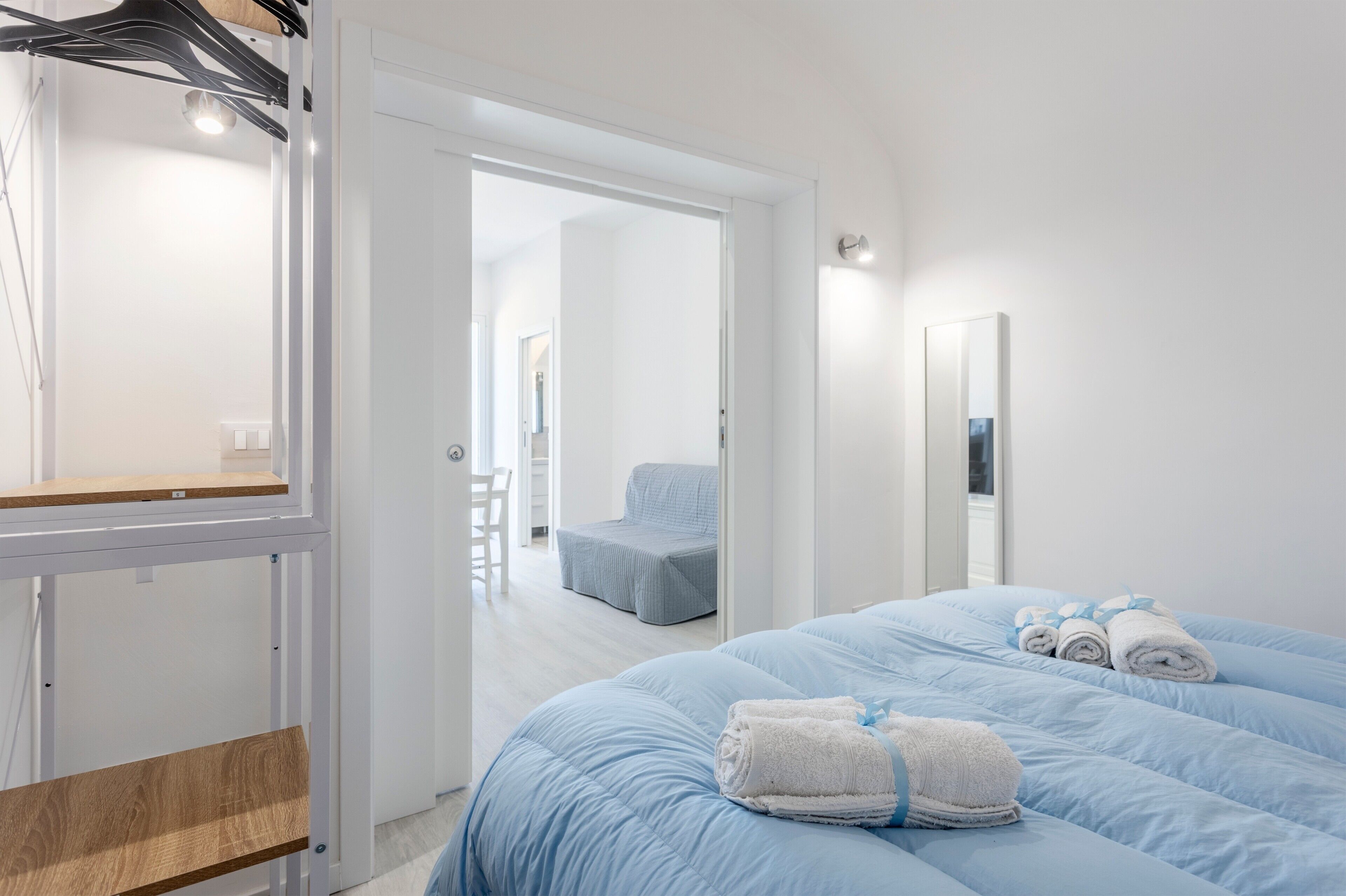 Una camera d'albergo con un letto, una sedia, uno specchio e una porta che dà su un'altra stanza.