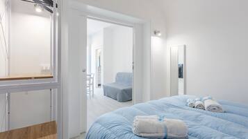 Una camera d'albergo con un letto, una sedia, uno specchio e una porta che dà su un'altra stanza.