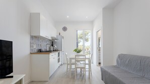 Une cuisine moderne avec des meubles blancs, une table à manger et un canapé gris.
