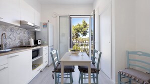 Une cuisine compacte avec un coin repas, une vue à travers une porte vitrée et un petit balcon.