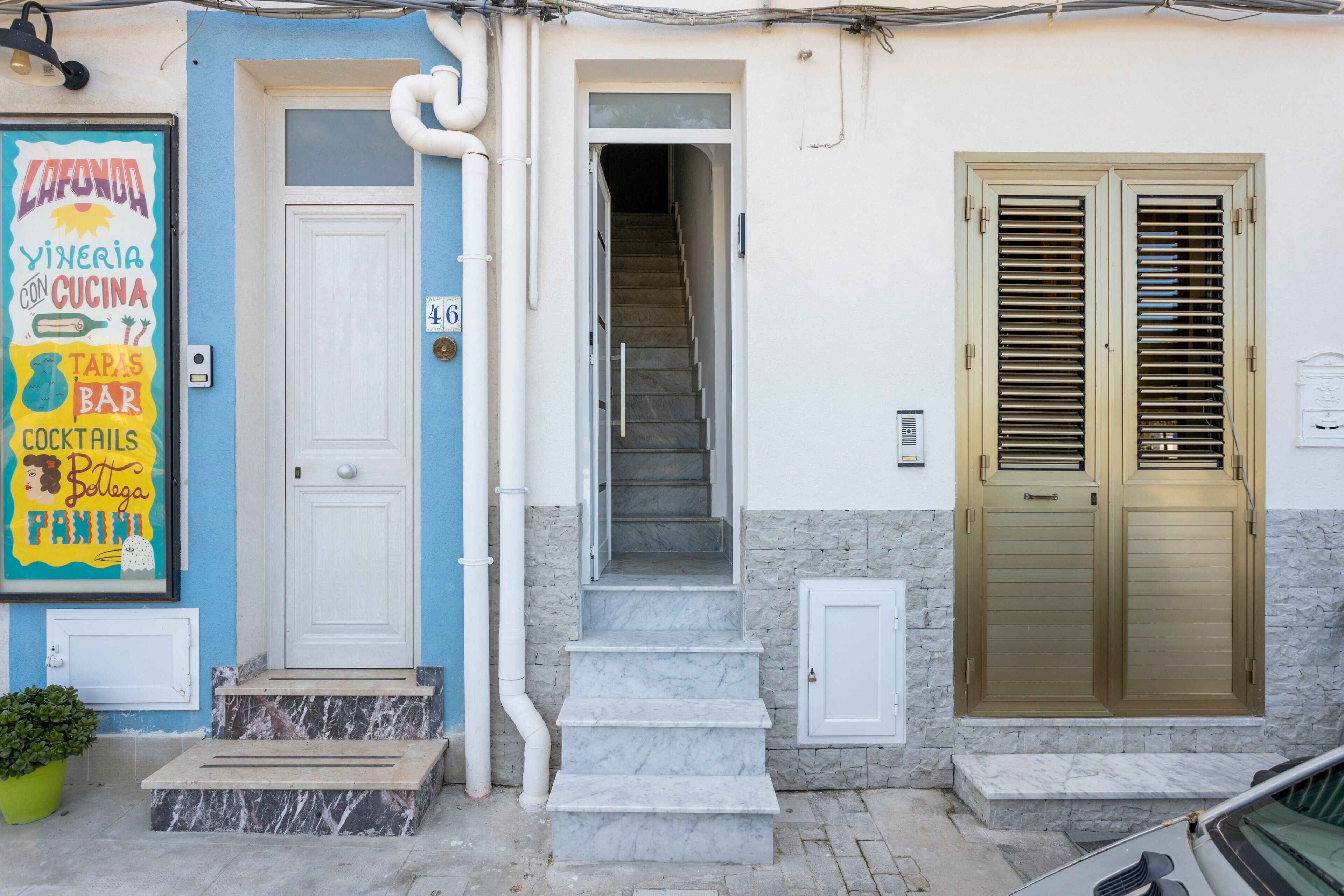 A building with a blue and white facade, a white door, a staircase, and a set of double doors with shutters.