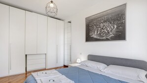 Un dormitorio con cama, armario blanco y una pintura de paisaje urbano.