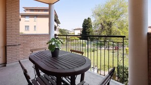 Un balcón con una mesa y sillas de madera redonda, una planta en maceta y vistas a una zona residencial con edificios y árboles.