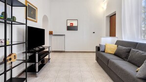 Un salon avec un téléviseur à écran plat, un canapé gris, une étagère noire et un tableau encadré accroché au mur.