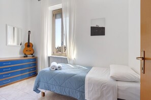 Un dormitorio con cama, cómoda, guitarra, ventana con cortinas e imagen colgada en la pared.