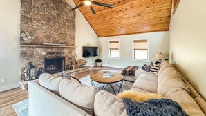 Un salon spacieux avec une cheminée en pierre, un plafond en bois et un grand canapé.